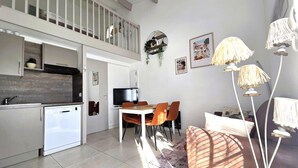 A compact kitchen with a dishwasher, a dining area with a table and chairs, a television, and a balcony with a railing.