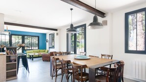 Een ruime eethoek met een houten tafel en stoelen, grote ramen en een blauwe accentmuur.