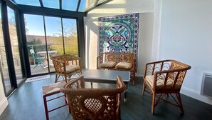 Habitación soleada con sillas de mimbre, puerta de cristal que da al exterior y una pared decorativa de azulejos.