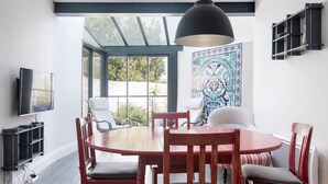 Un comedor con una mesa redonda de madera, sillas rojas, una lámpara colgante negra y un ventanal con vistas a zonas verdes.