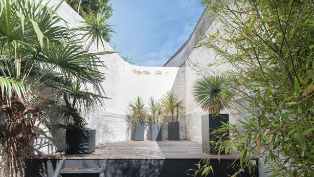 Un patio con terraza de madera, plantas en macetas y una escalera que lleva a un nivel superior.