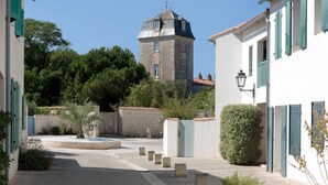 Una calle estrecha flanqueada por edificios, una torre al fondo y una pequeña fuente en el centro.