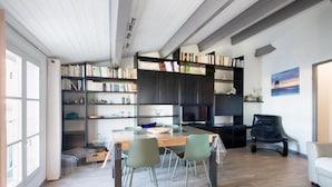 Un salon moderne avec une table à manger en bois, des chaises vertes, un fauteuil en cuir noir et une bibliothèque remplie de livres.