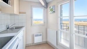 Une cuisine avec des meubles blancs, un four encastré et une fenêtre donnant sur une plage.