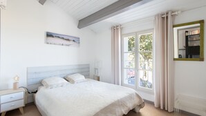 Une chambre à coucher comprenant un lit, une table de chevet, une commode, une fenêtre avec des rideaux et une étagère murale avec des livres.