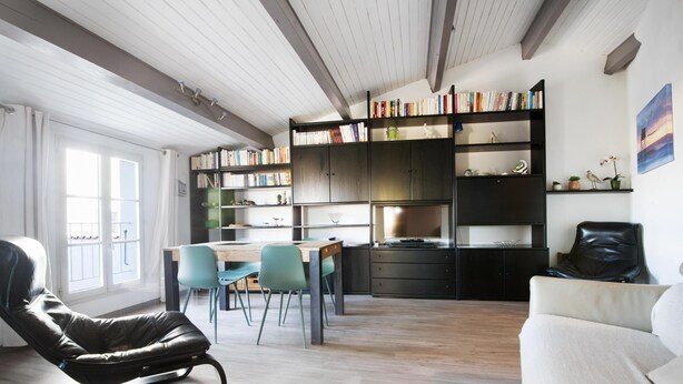 Un salon moderne comprenant un coin repas, un fauteuil en cuir noir, un canapé blanc et une bibliothèque remplie de livres.