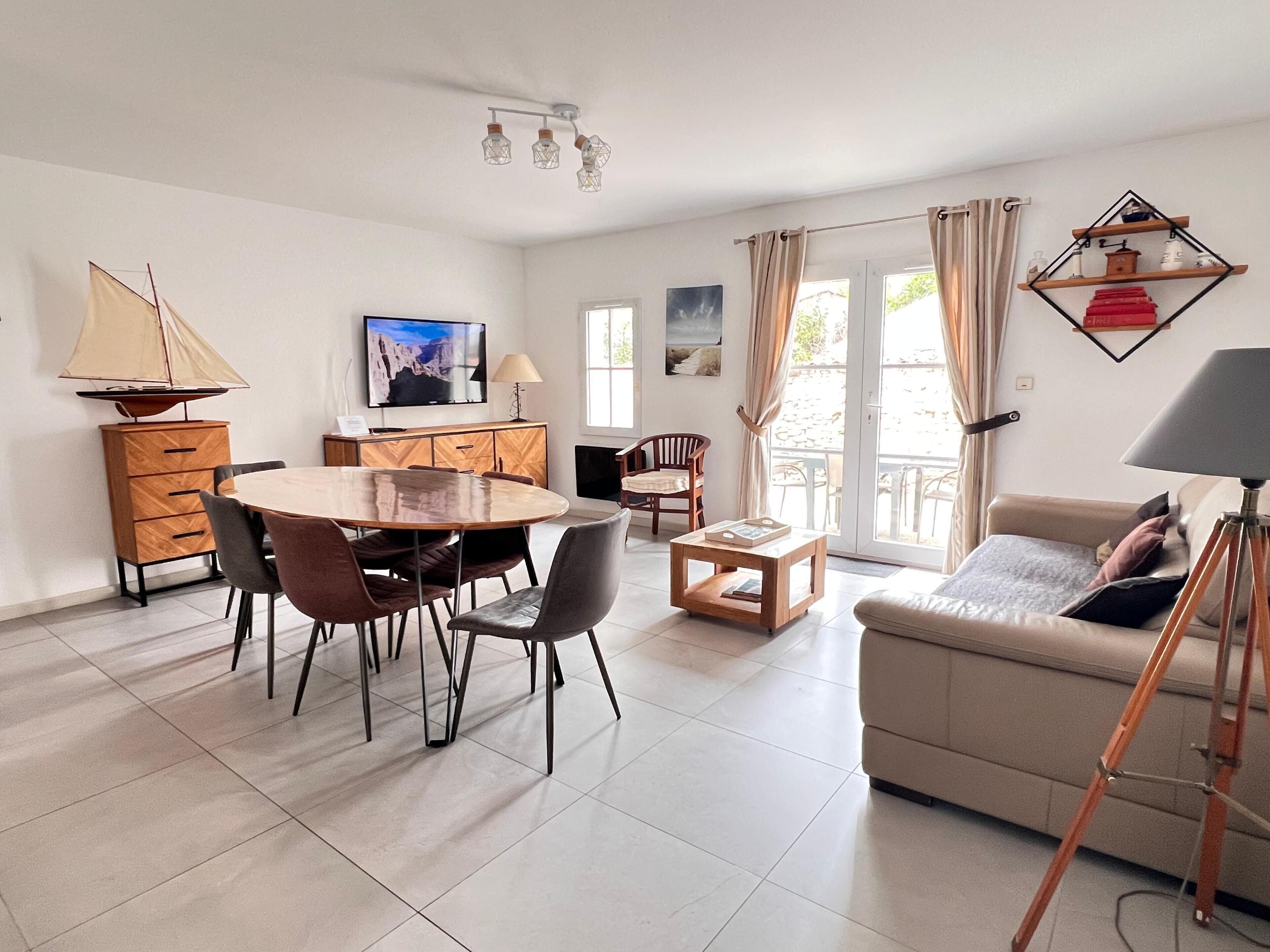 A modern living room with a round dining table, a sofa, a TV, and a sailboat model.