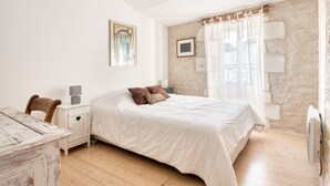 A bedroom with a bed, a desk, a chair, and a stone wall. - House SALICORNE    . (La Flotte)