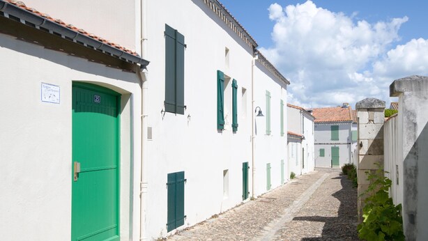 Eine enge Kopfsteinpflasterstraße, gesäumt von weißen Gebäuden mit grünen Türen und Fensterläden.