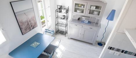 A modern kitchen with white cabinets, a blue dining table with chairs, and a coffee maker on a metal shelf.