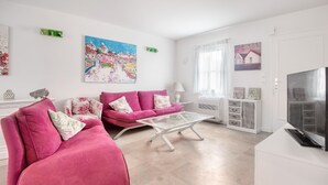 Un salon avec deux canapés roses, une table basse en verre, un meuble TV blanc et un tableau accroché au mur.