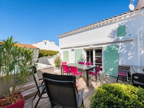 Eine Terrasse mit Tisch und Stühlen, einem Blumentopf und einem weißen Gebäude mit grünen Fensterläden.