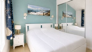 Une chambre avec un grand lit, une table de chevet, un miroir et des œuvres d’art murales.