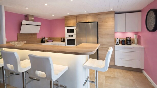 Une cuisine moderne dotée d’un îlot central, de tabourets de bar et d’un mur d’accent rose.