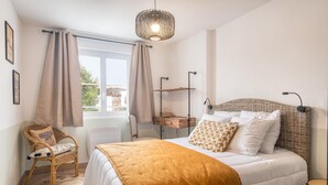 Ein Schlafzimmer mit Bett, einem Sessel, einem Nachttisch, einer Lampe und einem Fenster mit Vorhängen.