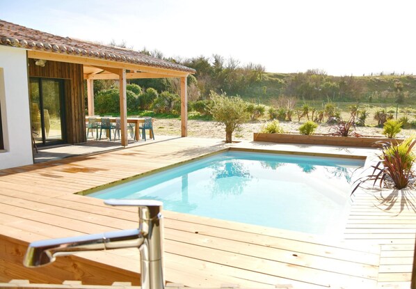 Eine Holzterrasse mit Pool, Sitzgelegenheiten im Freien und einem überdachten Bereich.
