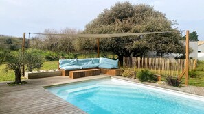 Eine Holzterrasse mit Pool, einem hellblauen Sofa und einer Pergola.