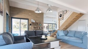 A modern living room with a large sofa, a coffee table, and a staircase with wooden railings. - DUNE               . (La Couarde-sur-Mer)