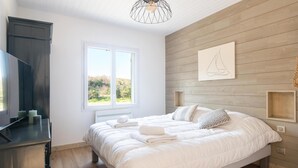A bedroom with a bed, a TV, a window, and a wooden wall with a sailboat artwork. - DUNE               . (La Couarde-sur-Mer)