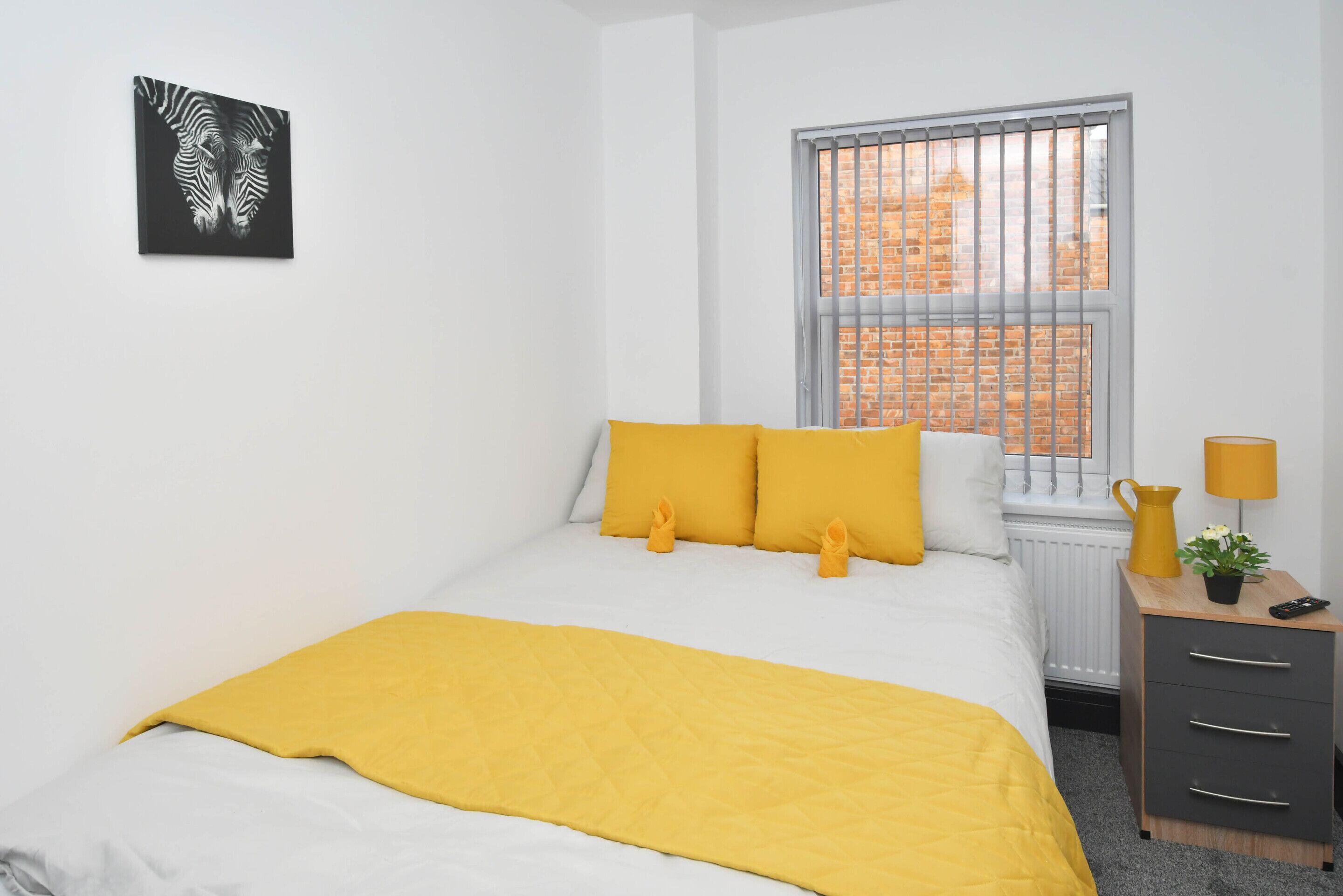Una camera da letto con un letto, una finestra con persiane, un comodino con una lampada e una piccola pianta.