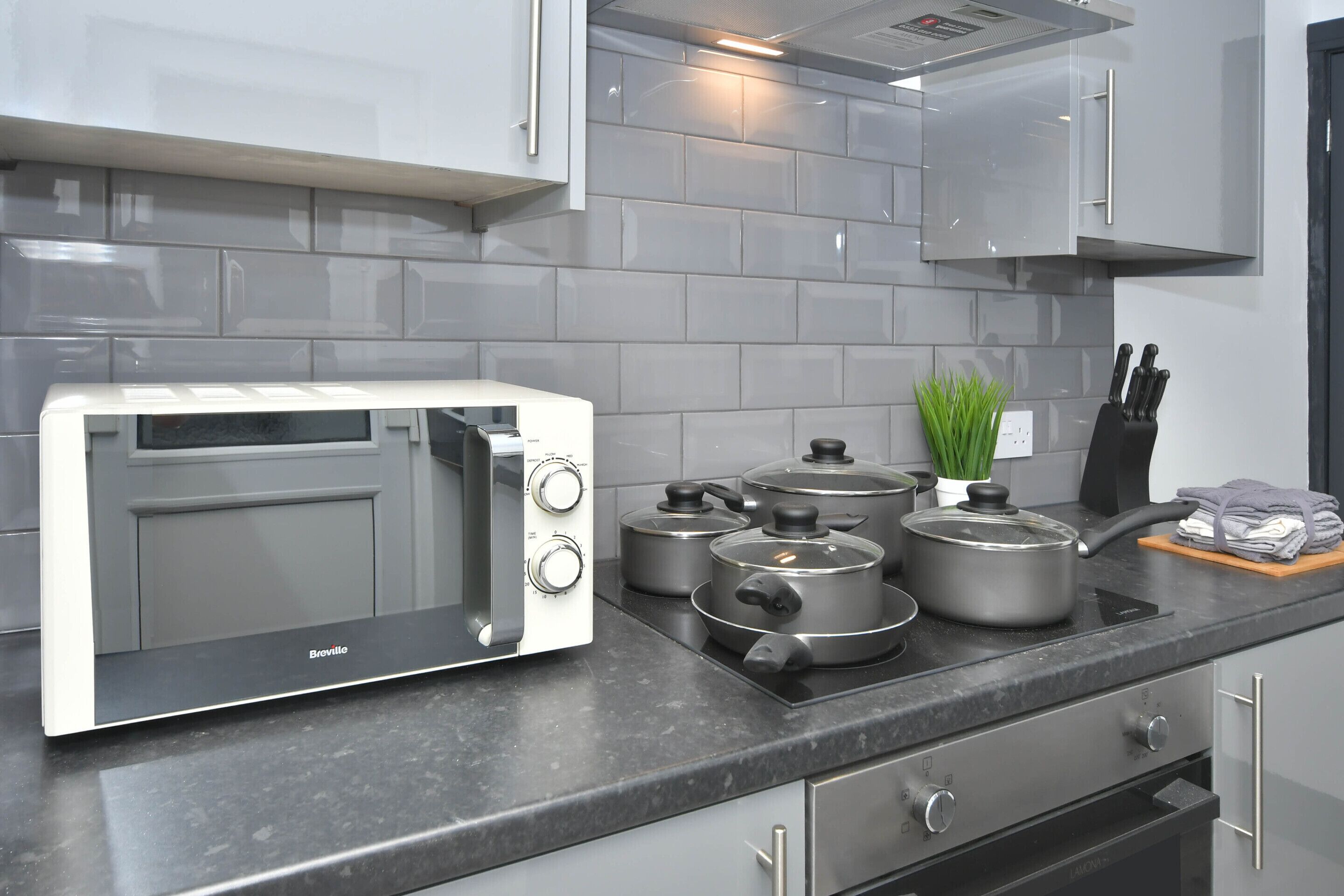 A modern kitchen with a Breville toaster oven, a stove with pots, a knife block, and a potted plant.