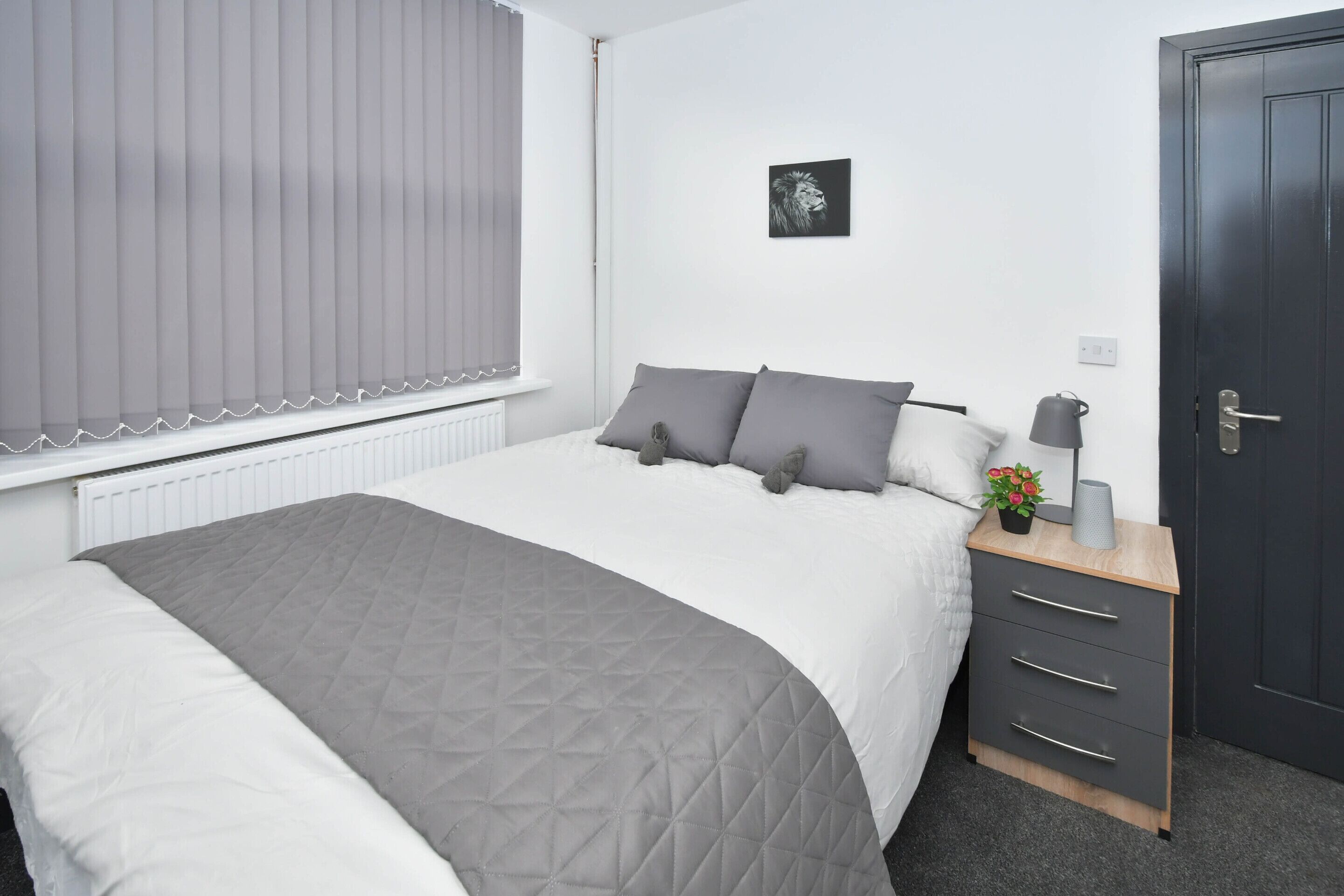 A bedroom with a bed, a bedside table with a lamp, a small plant, and a door.