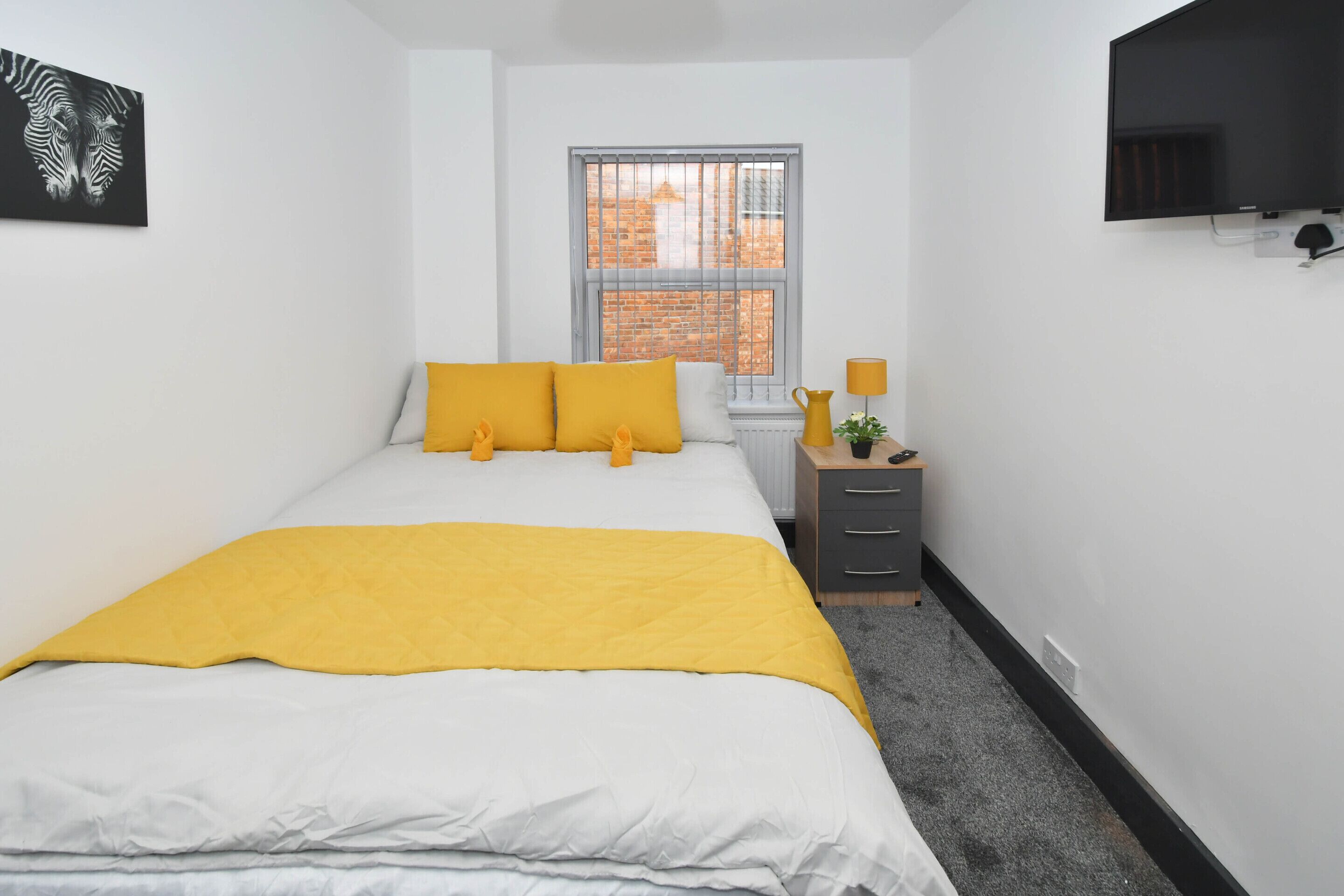 A bedroom with a bed, a window, a dresser, and a television.