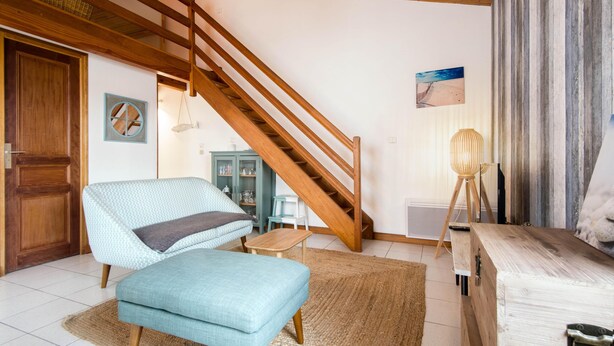 Un salon avec un escalier en bois, un canapé bleu, une petite table et une lampe.