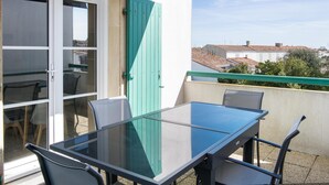 Une table à plateau en verre, entourée de chaises, sur un balcon extérieur, avec en arrière-plan une vue sur des maisons.
