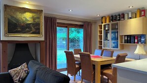 Ein gemütliches Wohnzimmer mit Kamin, ein Essbereich mit Holztisch und -stühlen sowie ein Bücherregal mit verschiedenen Gegenständen.
