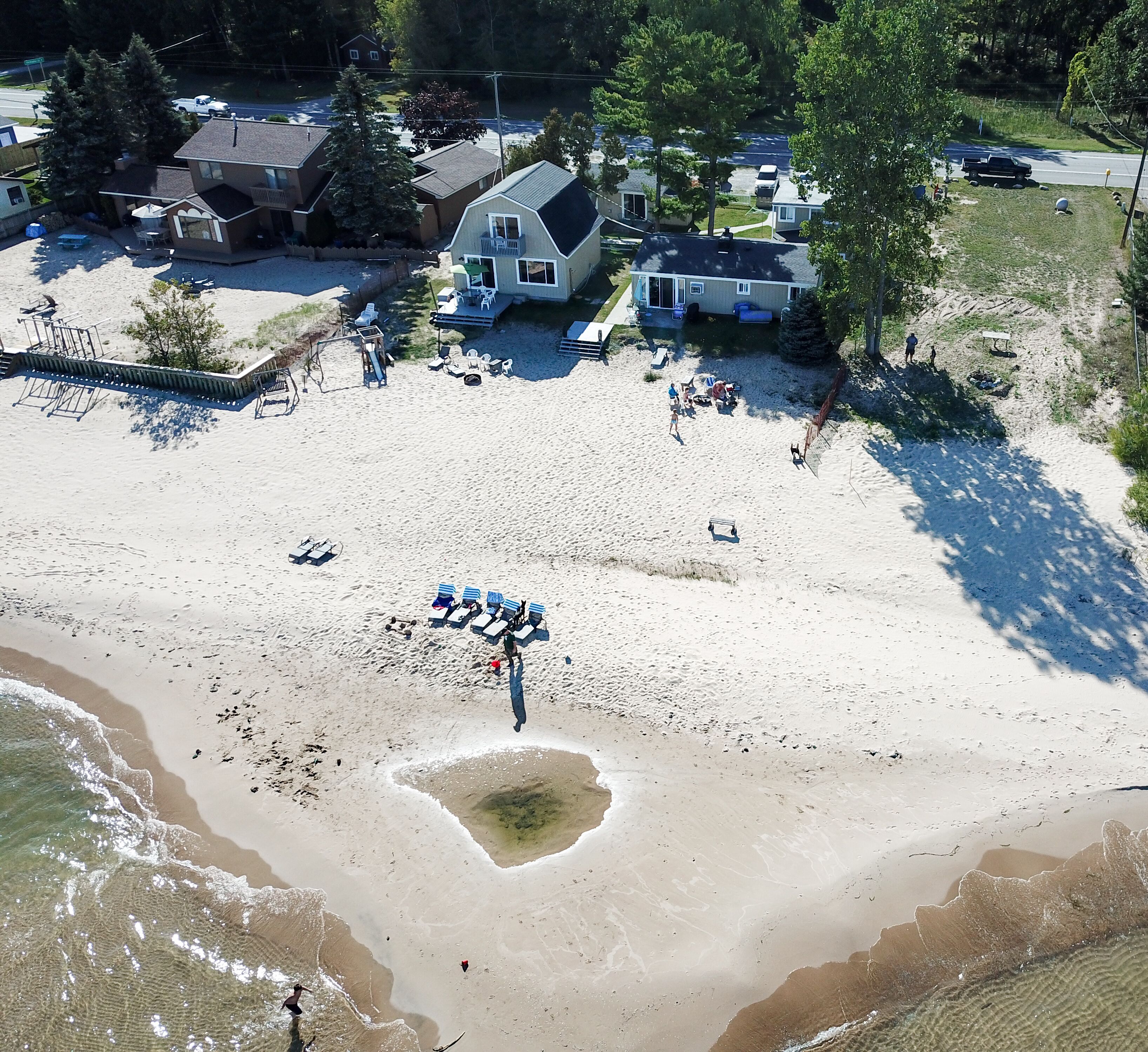An aerial view of a beach with a row of beach chairs and umbrellas, a small pool, and a building with a balcony.