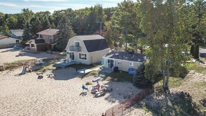 Une propriété située en bord de mer, comprenant une grande maison, une plage de sable et un espace clos aménagé avec du mobilier d’extérieur.