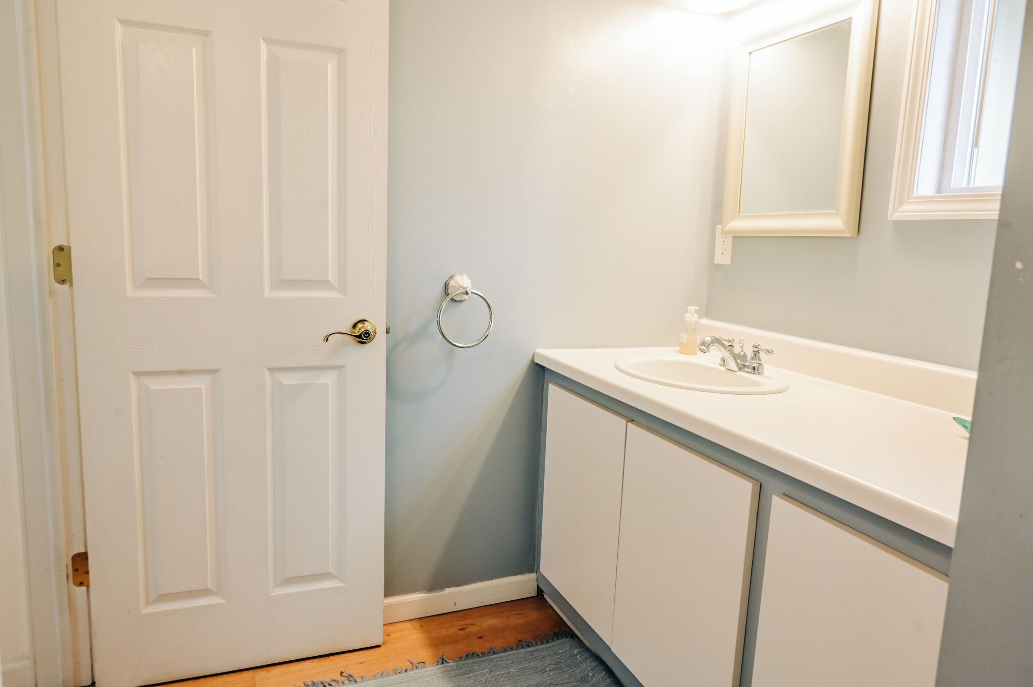Une salle de bain avec une porte blanche, un lavabo avec un miroir et un porte-serviettes fixé au mur.