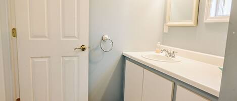 Une salle de bain avec une porte blanche, un lavabo avec un miroir et un porte-serviettes fixé au mur.