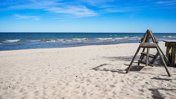 Une plage de sable avec une échelle en bois et une petite structure, probablement une chaise de plage ou une table, sous un ciel bleu dégagé.