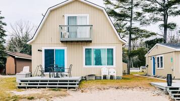 A two-story beach house with a balcony, a deck with chairs, and a small pool area.