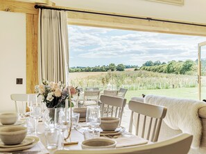 A dining table set with plates, glasses, and a vase of flowers, overlooking a grassy field. - 3 bedroom accommodation in Alresford (Alresford)