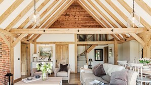 Un loft espacioso con vigas de madera a la vista, una zona de estar acogedora con sofá y sillones, una mesa de comedor y una escalera que sube a un nivel superior.
