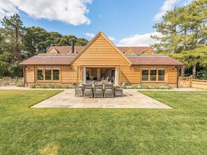 Une maison en bois dotée d’un patio, d’un coin repas et offrant une vue sur les arbres environnants.
