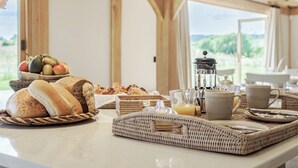 Una mesa con pan, pasteles, fruta y una cafetera para el desayuno.