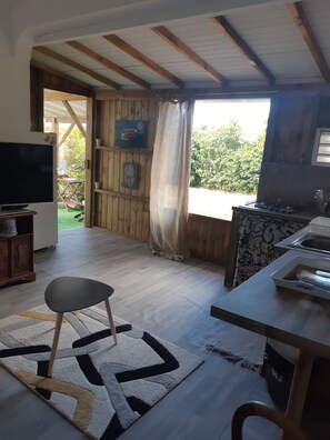 Uma cozinha rústica com vigas de madeira, uma janela grande com cortinas, uma televisão e um espaço de jantar com tapete.