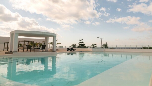 A swimming pool with a covered seating area and lounge chairs.