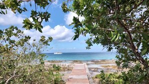 A wooden pathway leading to a beach with a sailboat in the distance.