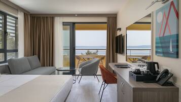 Una habitación de hotel con cama, escritorio con teléfono, una silla, un sofá y un balcón con mesa y sillas.