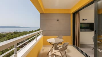 Ein Balkon mit Tisch und Stühlen, Blick aufs Meer und eine Glastür zu einem Zimmer.