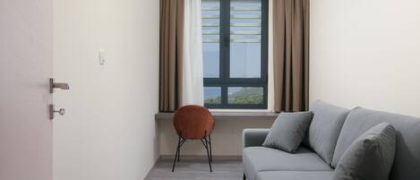 Ein modernes Wohnzimmer mit einem grauen Sofa, einem braunen Sessel, einem Fenster mit Vorhängen und einer Tür.