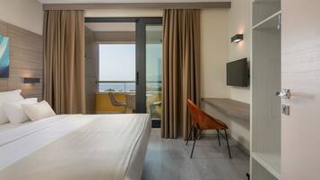 Habitación de hotel con cama, televisión, escritorio y balcón con vistas.