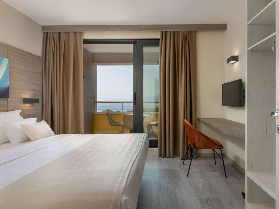 Habitación de hotel con cama, televisión, escritorio y balcón con vistas.
