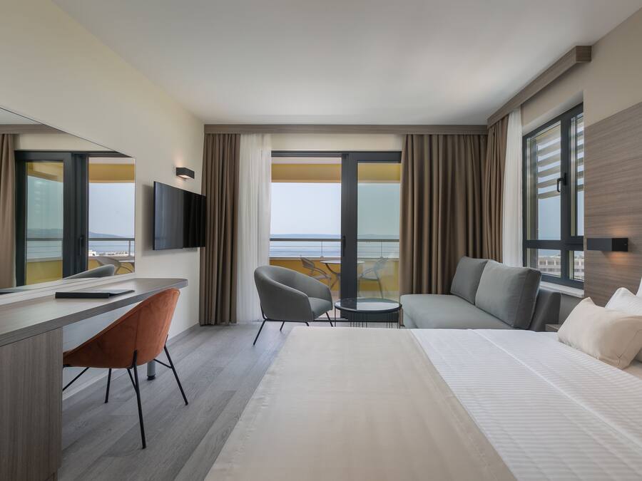 Una habitación de hotel moderna con una cama grande, un escritorio, una silla, un sofá y un televisor.