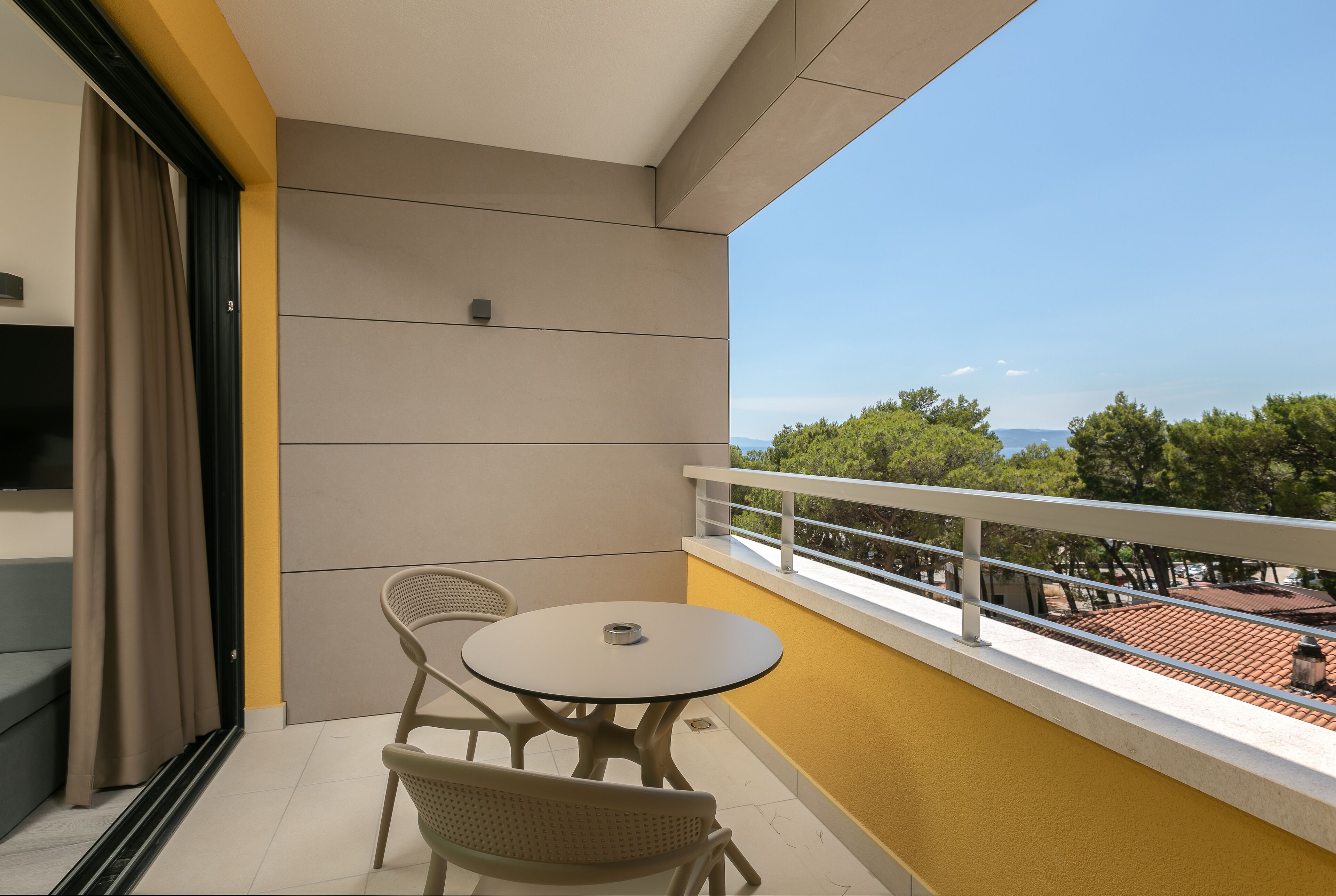 A balcony with a table and chairs, a sliding door, and a view of trees and buildings.